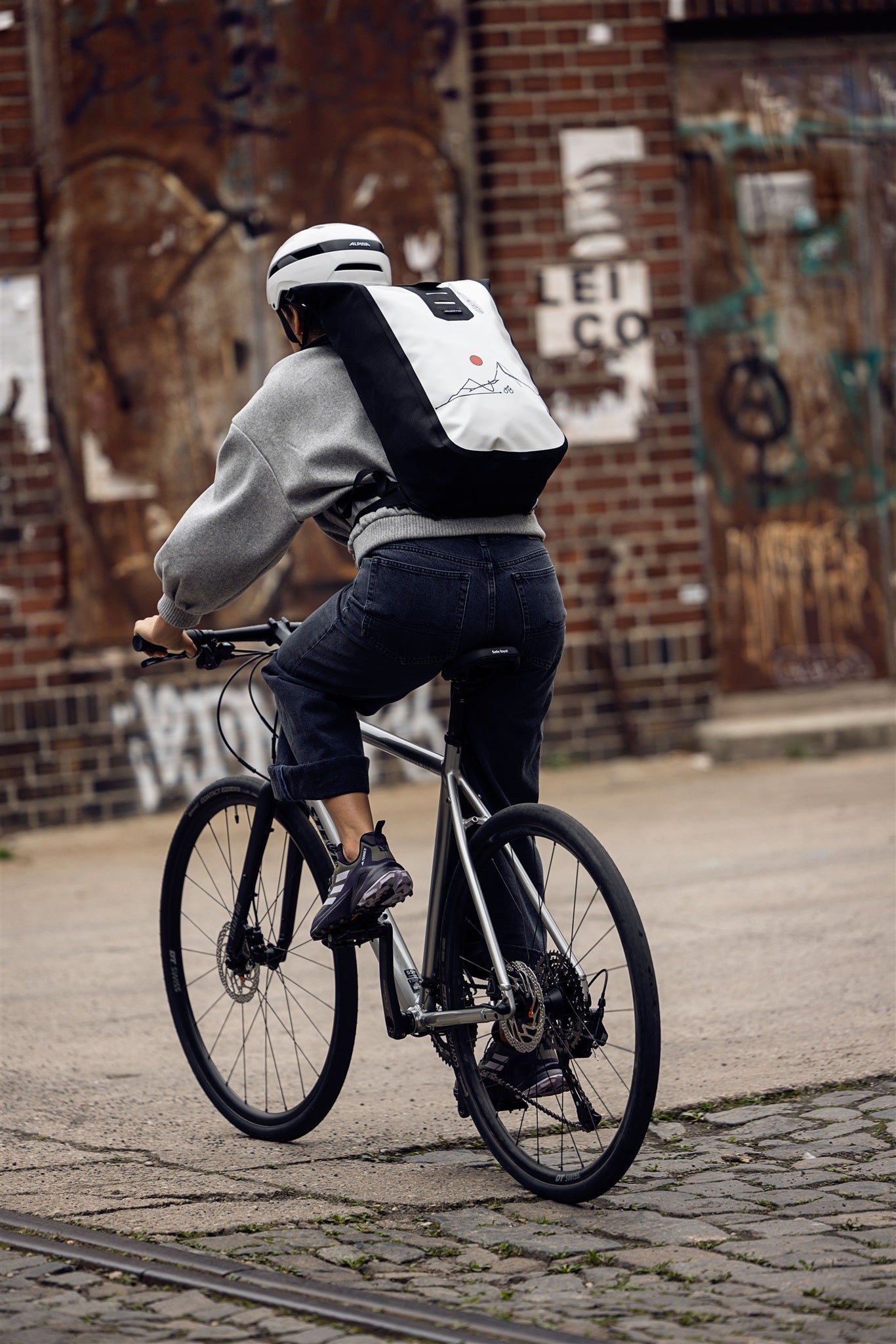 Vrouw zit op metalen trap met wit-zwarte ORTLIEB Velocity Design rugzak met rode zon