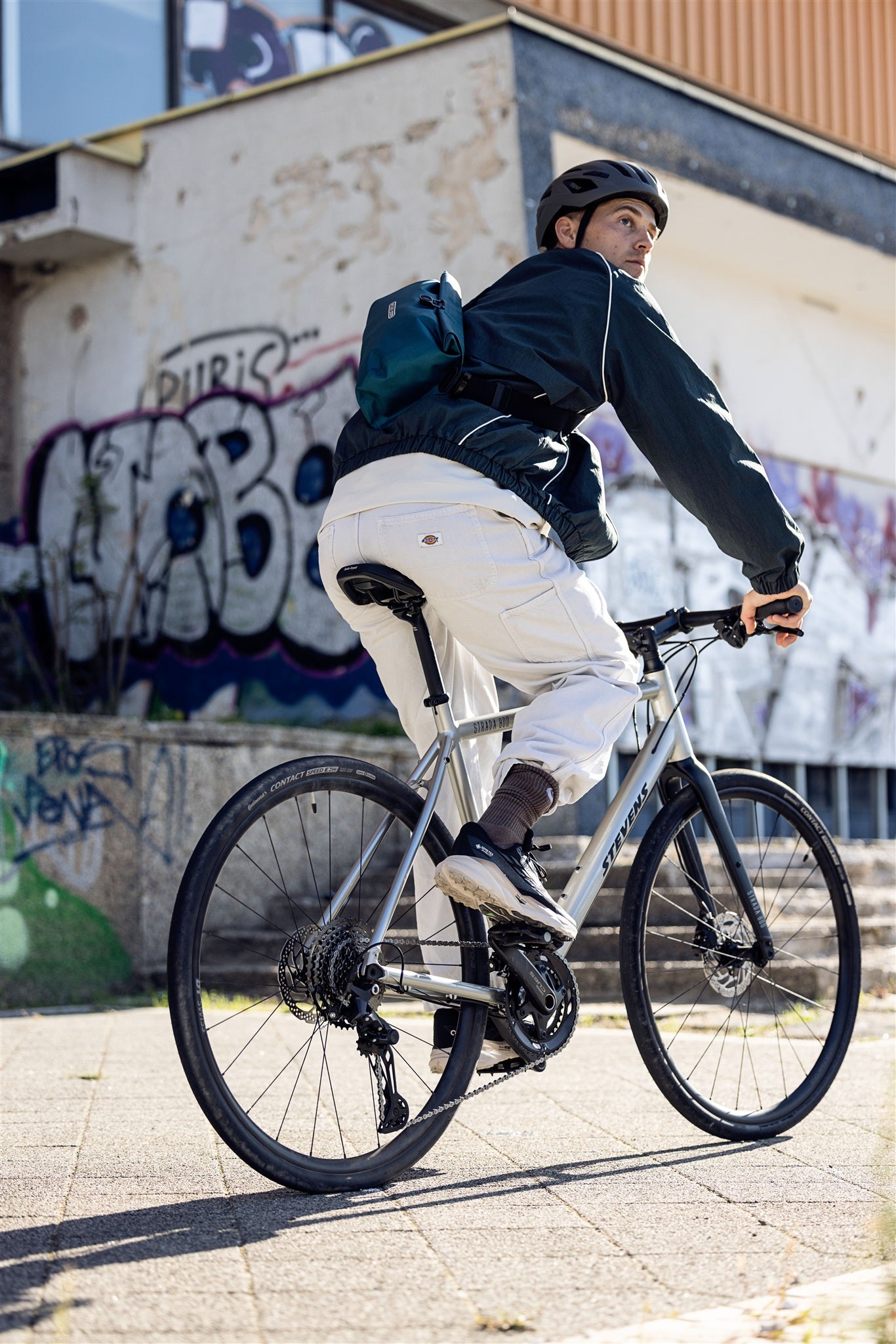 Fietser met petrol ORTLIEB Velo-Sling Flex heuptas in stedelijke omgeving met graffiti.